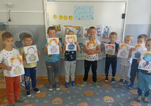 Dziewięć chłopców stoi na tle białej tablicy z wykonaną pracą plastyczną.