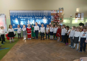 Grupa dzieci stoi na tle dekoracji.