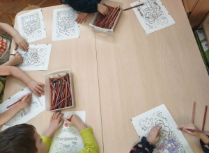 dzieci siedzą przy stoliku i kolorują kolorowanki z okazji Dnia Babci i Dziadka