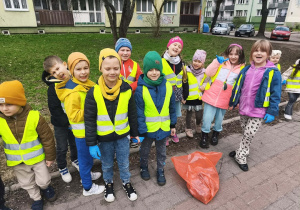 Dzieci stoją na chodniku. Przed nimi leży czerwony worek.