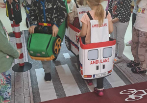 Dzieci przebrane za pojazdy poruszają się po dywanie z nadrukowaną ulicą