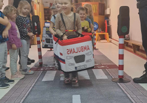 Dzieci przebrane za pojazdy poruszają się po dywanie z nadrukowaną ulicą