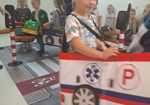 Dzieci przebrane za pojazdy poruszają się po dywanie z nadrukowaną ulicą