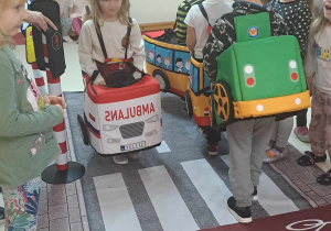 Dzieci przebrane za pojazdy poruszają się po dywanie z nadrukowaną ulicą