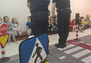 Przedstawiciele Straży Miejskiej stoją tyłem i przypominają dzieciom zasady bezpoeczęństwa
