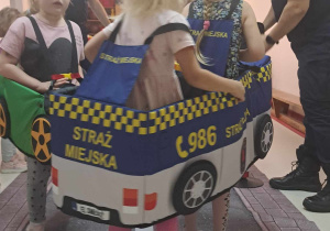 Dzieci przebrane za pojazdy poruszają się po dywanie z nadrukowaną ulicą