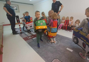 Dzieci przebrane za pojazdy poruszają się po dywanie z nadrukowaną ulicą