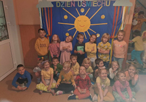 Grupa dzieci uśmiecha się do zdjęcia w tle dekoracja słońce i napis Dzień Uśmiechu