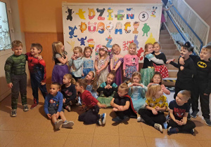 Grupa dzieci w strojach postaci z bajek pozuje do zdjęcia na tle dekoracji tematycznej