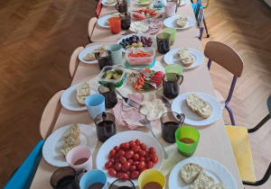 Nakryty stół - talerze, szklanki, owoce, warzywa, szynka, ser