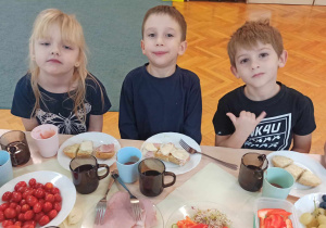 Dzieci siedzą przy stolikach i jedzą samodzielnie przygotowane kanapki
