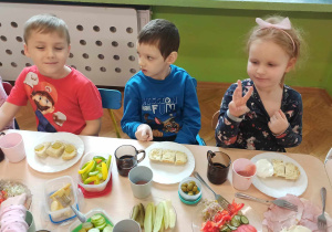 Dzieci siedzą przy stolikach i jedzą samodzielnie przygotowane kanapki