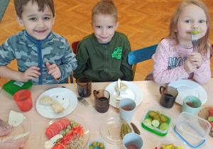Dzieci siedzą przy stolikach i jedzą samodzielnie przygotowane kanapki