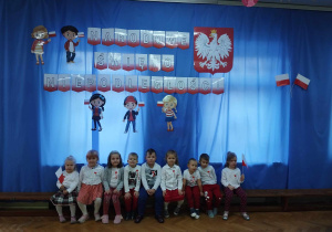 Dzieci ubrane w kolory biało- czerwone pozują na tle dekoracji w sali.