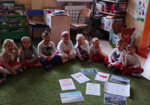 Dzieci siedza na dywanie i oglądają symbole narodowe.