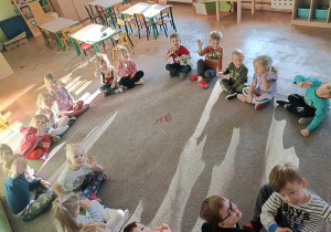 Dzieci siedzą na dywanie w kole i pozują do zdjęcia.