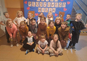 Grupa dzieci pozuje do zdjęcia na tle napisu Dzień Pluszowego Misia
