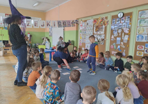 Dzieci siedzą w kole, chłopiec wróży z butelki