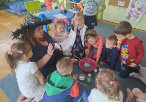 Dzieci siedzą na dywanie i z uwagą słuchają przepisu na mikstuę