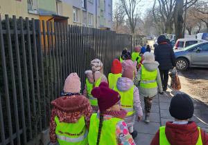 Dzieci w odblaskowych kamizelkach idą parami po chodniku