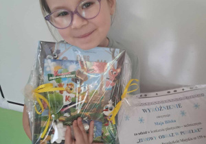 Dziewczynka prezentuje do zdjecia nagrodę i dyplom zdobyty w konkursie plastycznym