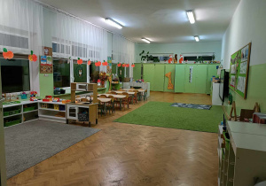 Sala przedszkolna. Po prawej stronie półki, po lewej stoliki.