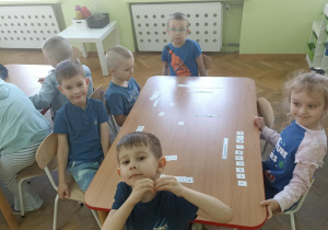 Piątka dzieci siedzi przy stoliku i układa napis z białych kartoników.