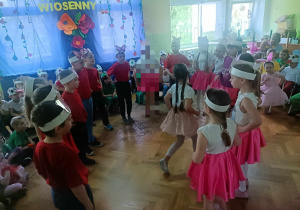 Dzieci w czerwonych koszulkach i różowych spódniczkach tańczą w kole.