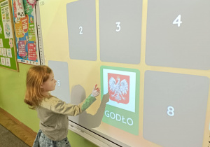 Dziewczynka otworzyła kartę w grze memory. Jest to symbol Polski-godło.