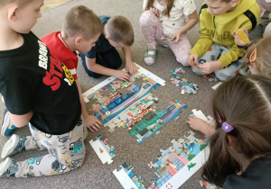 Wokół puzzli siedzi szóstka dzieci, które układają obrazek.