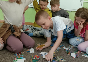 Chłopiec w białej bluzce łączy ze sobą dwa elementy. Z tyłu siedzi piątka dzieci.