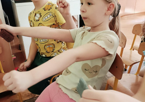 Dziewczynka w bluzce w serduszka udaje, że pilotuje samolot. W tle widać chłopca w żółtej koszulce, który uśmiecha się do zdjęcia.