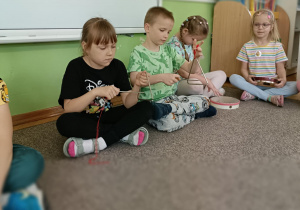 Czwórka dzieci siedzi na szarym dywanie i gra na instrumentach.