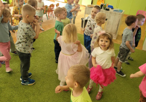 Dzieci tańczą na zielonym dywanie.