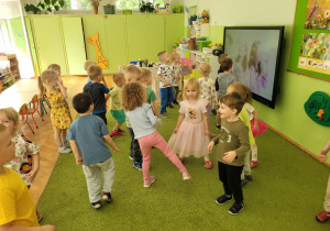 Dzieci tańczą na zielonym dywanie.