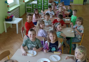 Dzieci siedzą przy stoliku i przygotowują poczęstunek.