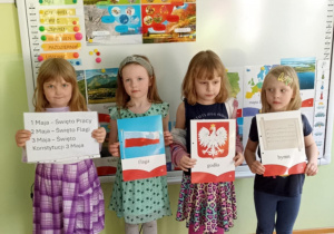 Cztery dziewczynki stoją na dywanie w sowy i pozują do zdjęcia z symbolami narodowymi.