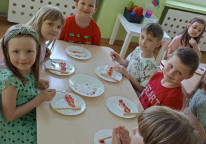 Dzieci siedzą przy stoliku i przygotowują poczęstunek.