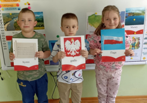 Dwóch chłopców i jedna dziewczynka pozują do zdjęcia z symbolami narodowymi.