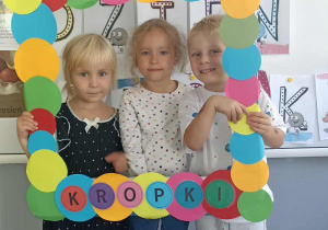 Dwie dziewczynki i chłopiec stoją w ramce z napisem Dzień Kropki.