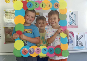 Trzech chłopców stoi w ramce z napisem Dzień Kropki.