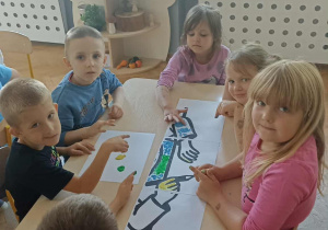 Szóstka dzieci siedzi przy stoliku i maluje farbami kropkową pracę plastyczną.