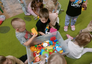 Dwóch chłopców siedzi wokół dużego, przezroczystego pudełka z klockami
