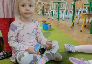 Dziewczynka w różowej sukience siedzi na dywanie w siadzie skrzyżnym a w rękach trzyma zwierzątka