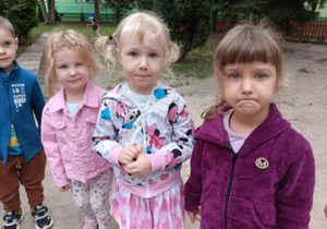 Trzy dziewczynki stoją w ogrodzie przedszkolnym.