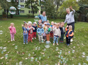 Dzieci stoją na trawie wraz z Paniami i uśmiechają się do zdjęcia.