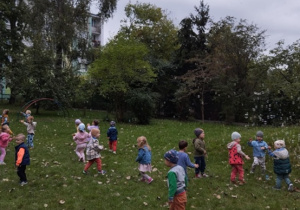 Dzieci biegają po trawie i łapią bańki mydlane.