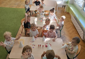 Trzy stoliki przy których siedzą dzieci. W tle widać kącik z zabawkami.
