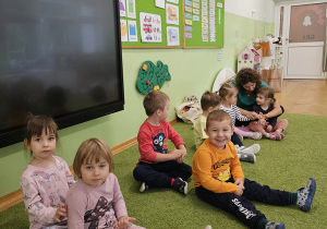 Dzieci wykonują masaże pleców siedząc na zielonym dywanie.