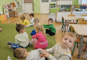 Dzieci wykonują masaże pleców siedząc na zielonym dywanie.